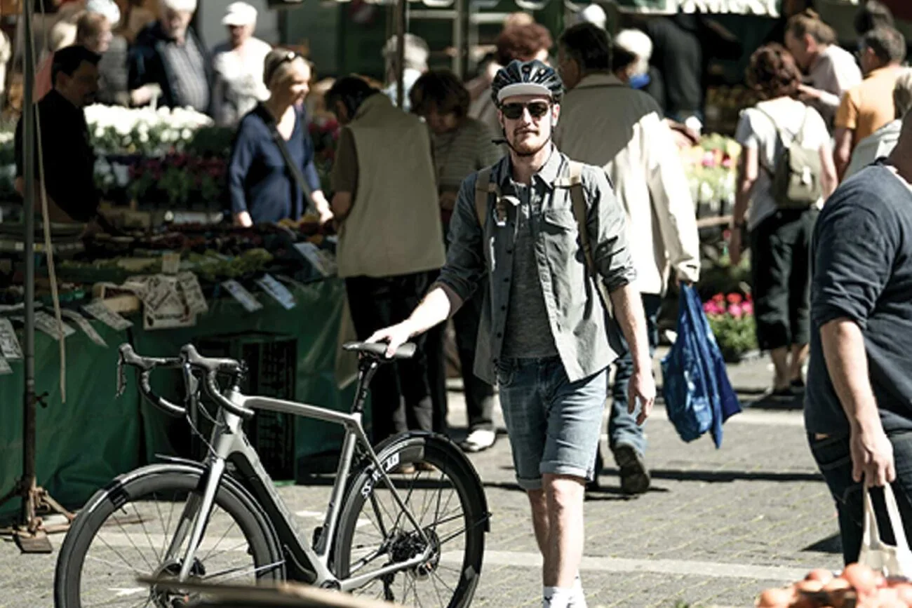 Fahrradfahrer schlendert mit seinem Gravel-Bike von Velocultour über einen Markt in einer Stadt.
