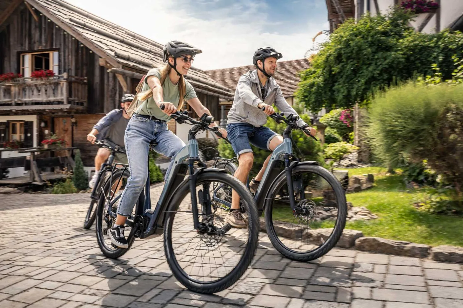 Drei Radfahrer auf blauem E-Bikes von Focus verlassen die Ausfahrt eines Bauernhofes.