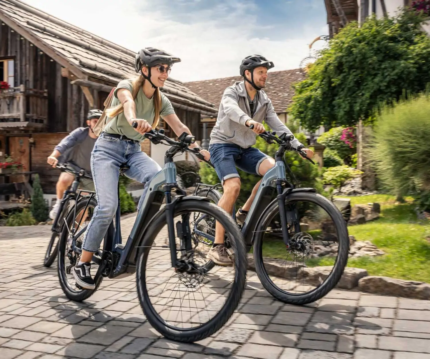 Drei Radfahrer auf blauem E-Bikes von Focus verlassen die Ausfahrt eines Bauernhofes.